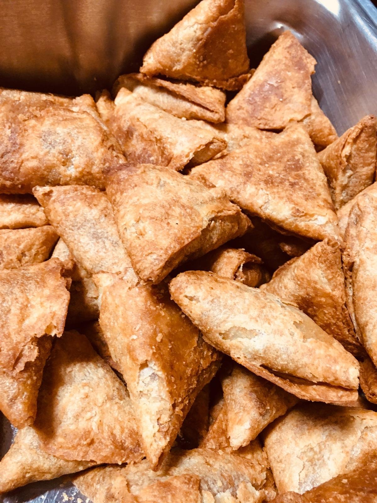 Fried samosas piled on a tray.