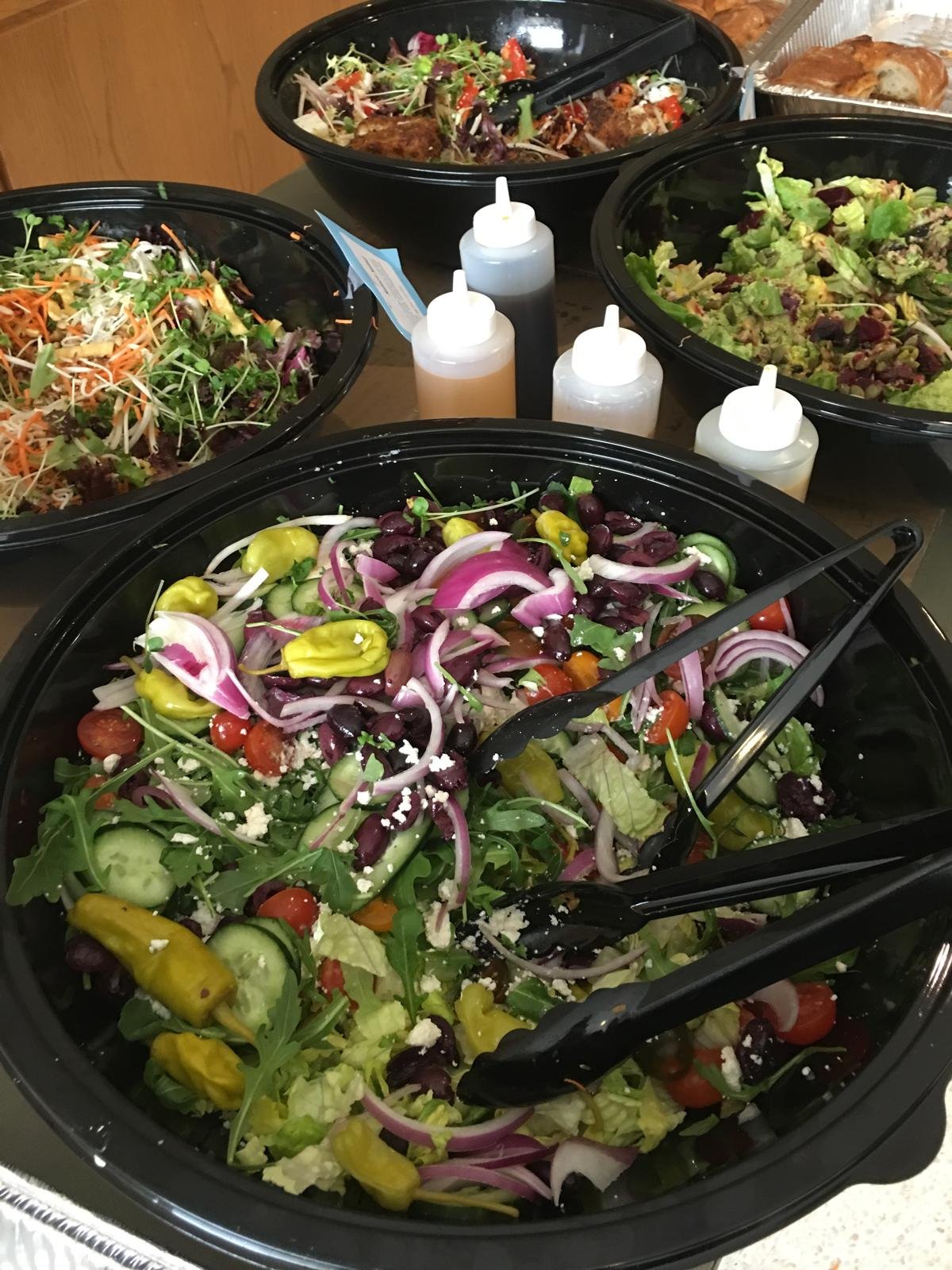 A dressed salad bowl with tongs beside squeeze bottles of dressing.