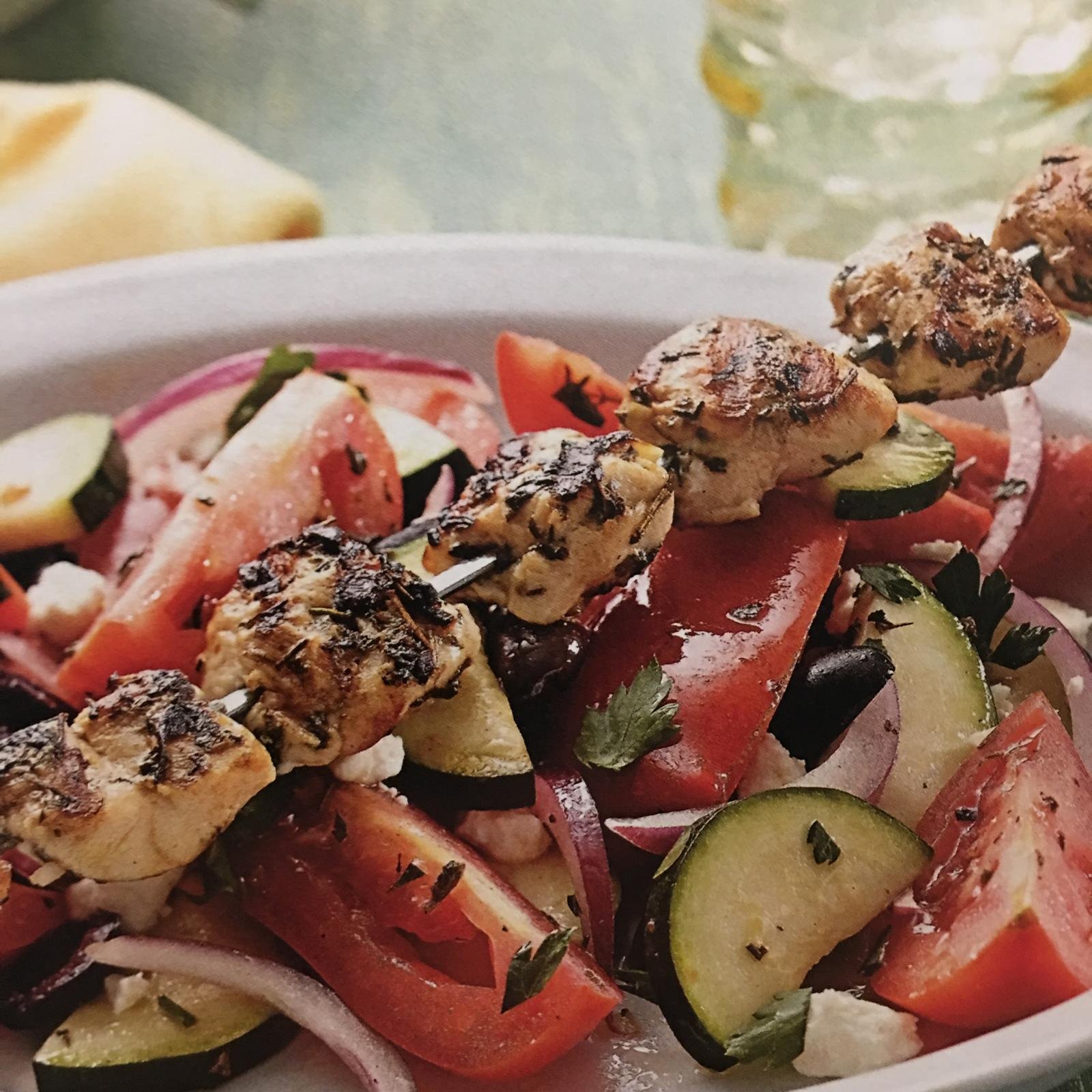 Grilled chicken skewers over a tomato and cucumber salad.