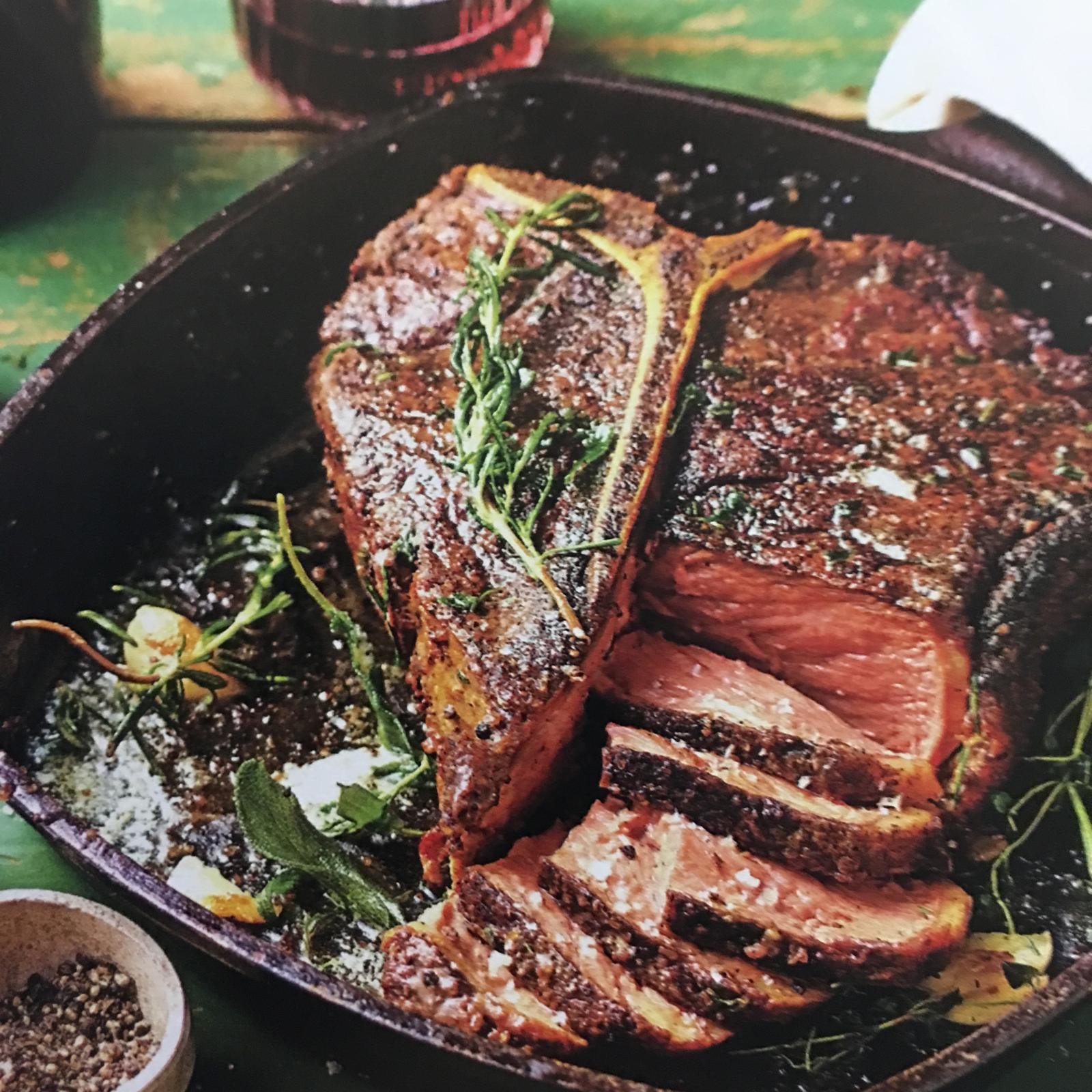 A steak resting in a cast-iron pan with herbs.