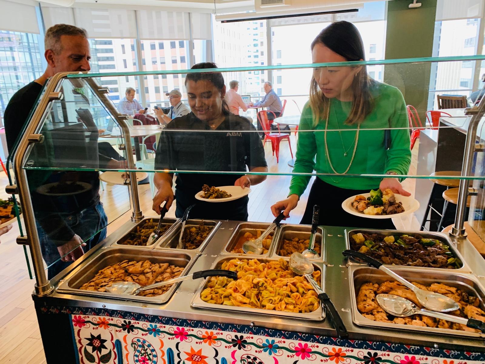 Colleagues serving themselves from chafing trays of chicken, noodles and vegetables at a buffet.