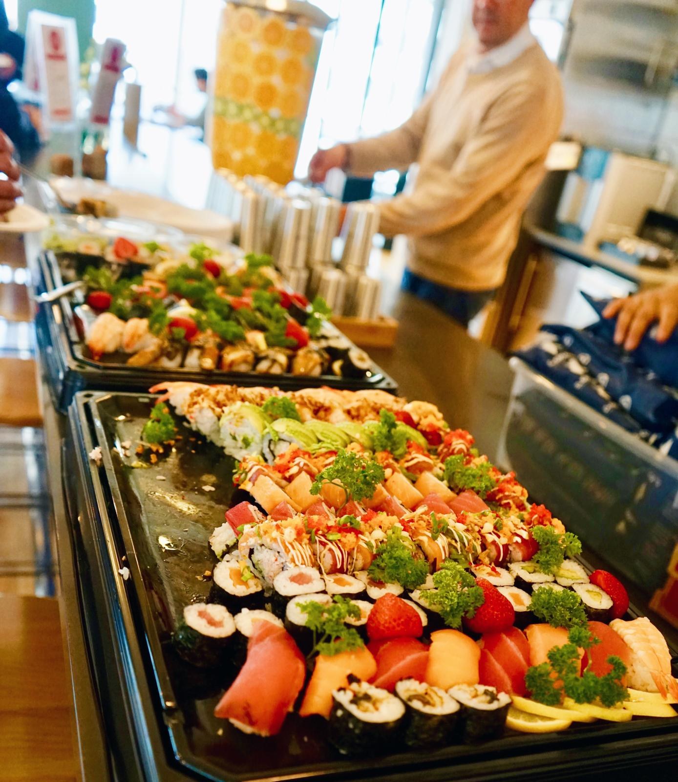 Sushi rolls and platters garnished with strawberries down a long office table.