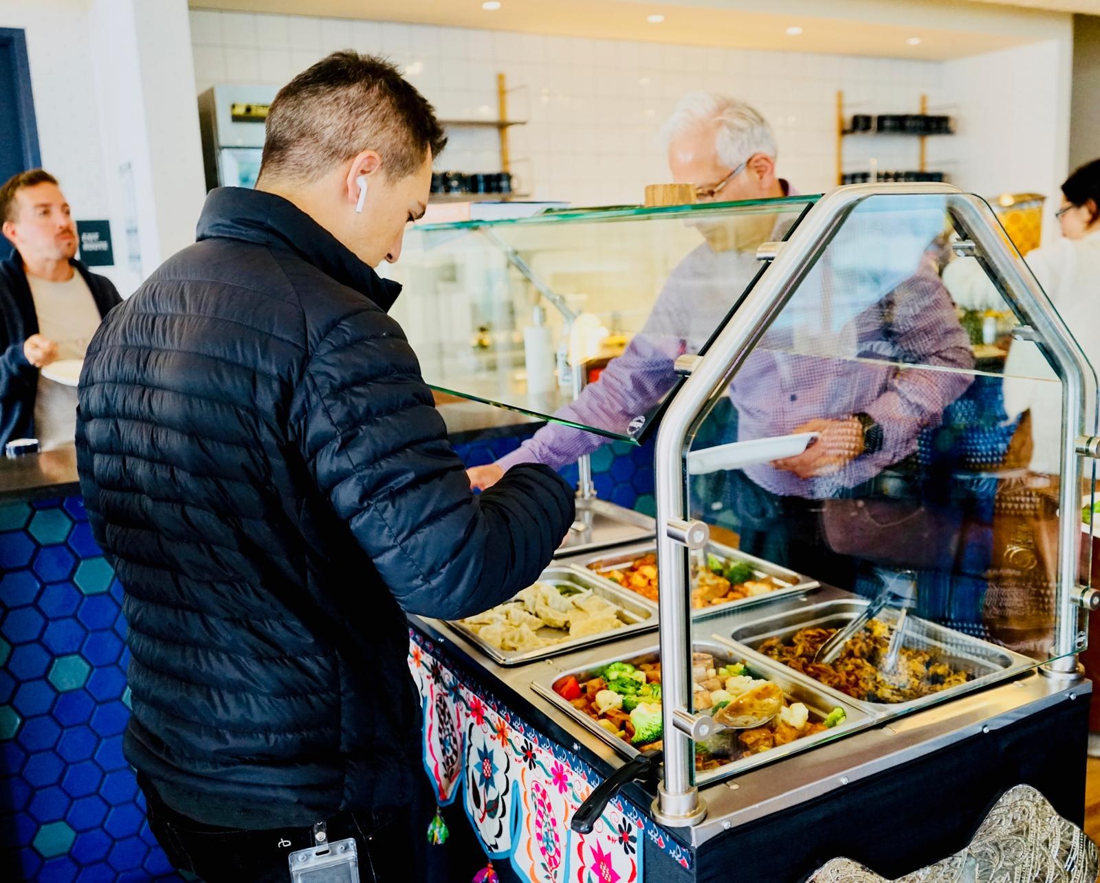 A man filling his plate at a glass-covered buffet cart.