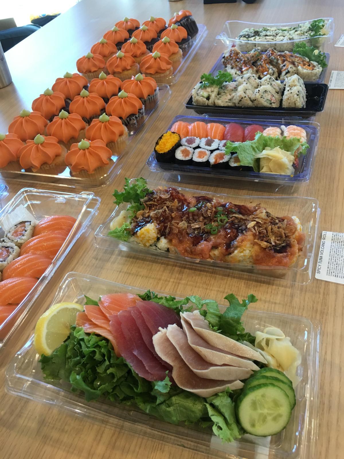Sushi trays, sashimi and a garnished roll platter laid across a table.