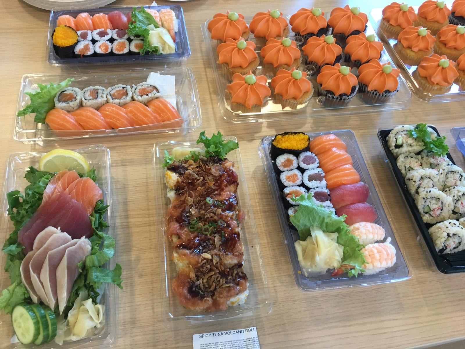 Sushi trays, sashimi and pumpkin-frosted cupcakes across a table.