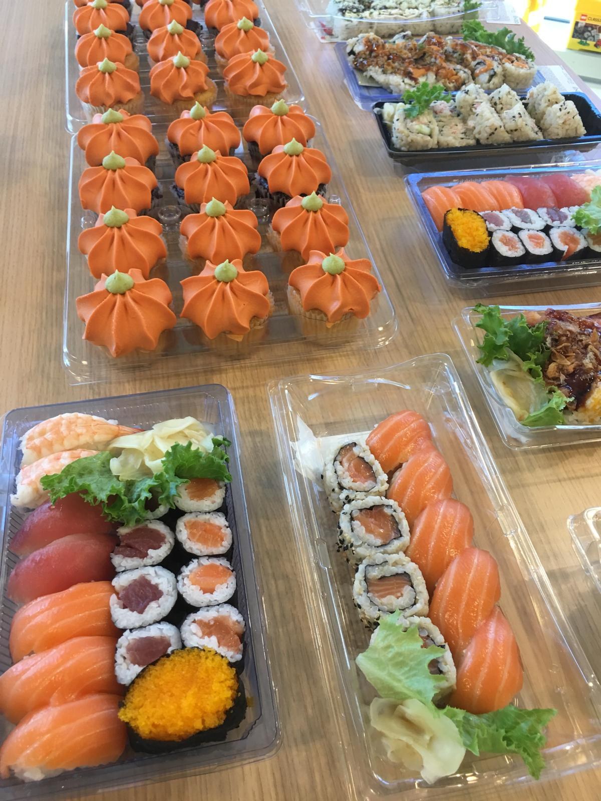 Pumpkin-frosted cupcakes beside trays of sushi rolls and sashimi.